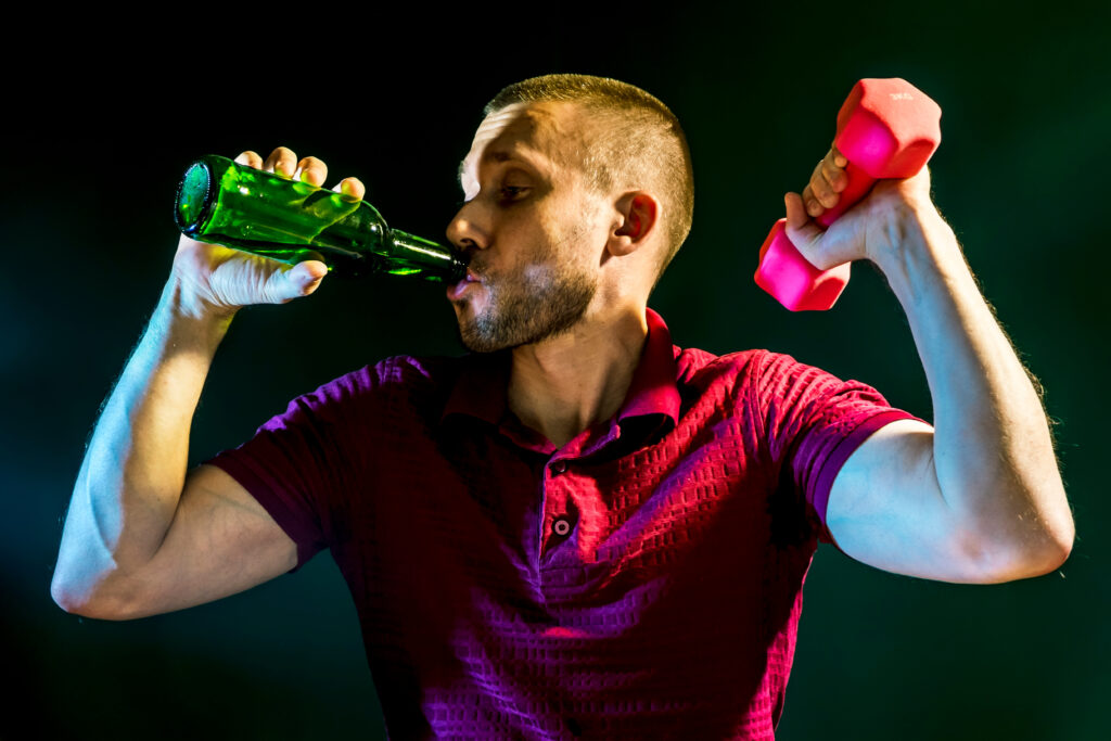 Man in a red shirt demonstrating temptation bundling by lifting a small weight while drinking.